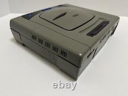 Console Sega Saturn en bon état avec manette grise, manuel et boîte testée.